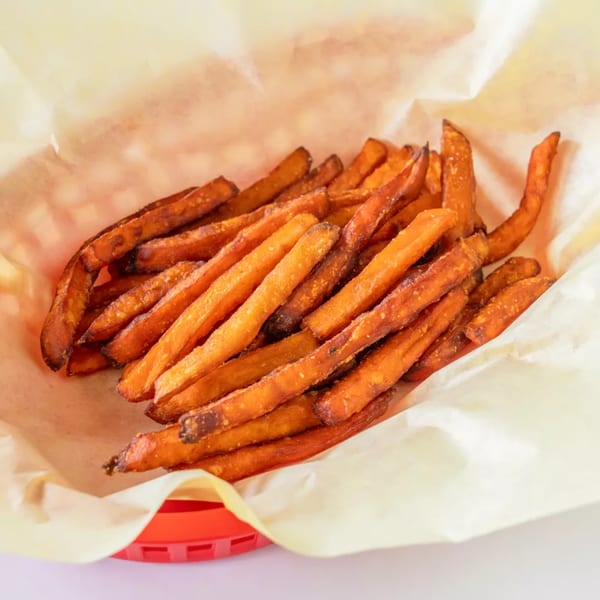 A red basket filled with crispy, golden-brown sweet potato fries lined with parchment paper.