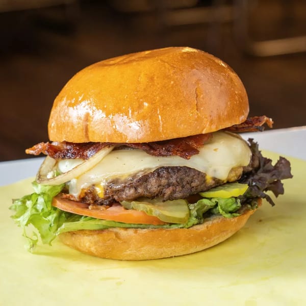 A juicy cheeseburger with bacon, grilled onions, lettuce, tomato, and pickles on a brioche bun.