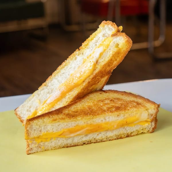 Two halves of a grilled cheese sandwich with melted orange and white cheese on a yellow surface.