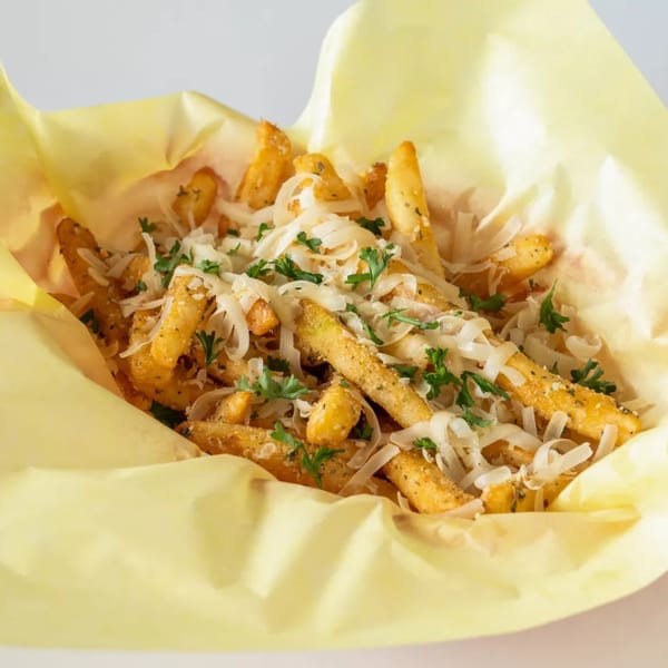 Golden french fries topped with shredded white cheese and green herbs in a yellow paper container.