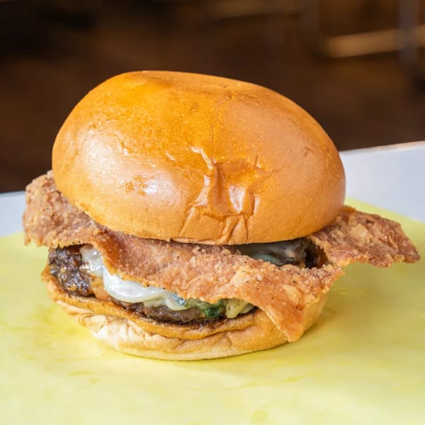 A close-up of a burger with a golden bun, melted cheese, and a crispy fried chicken patty.