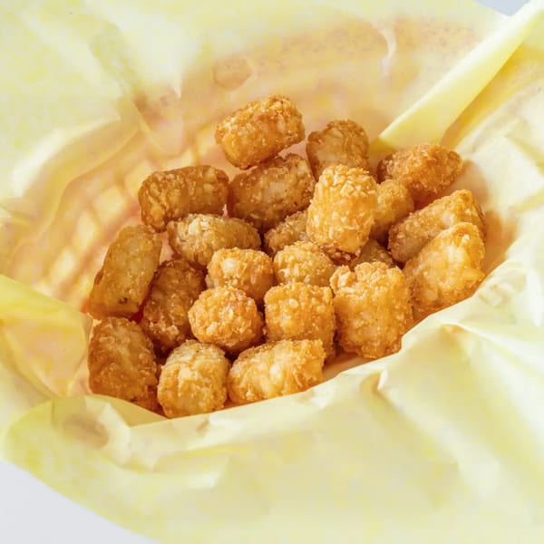Golden brown tater tots in a yellow paper-lined basket, ready to be served.