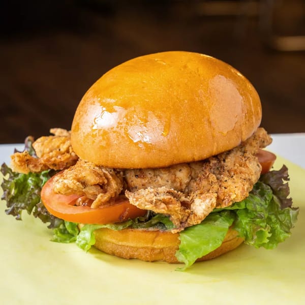 Crispy fried chicken sandwich with lettuce and tomato on a brioche bun, on a yellow surface.
