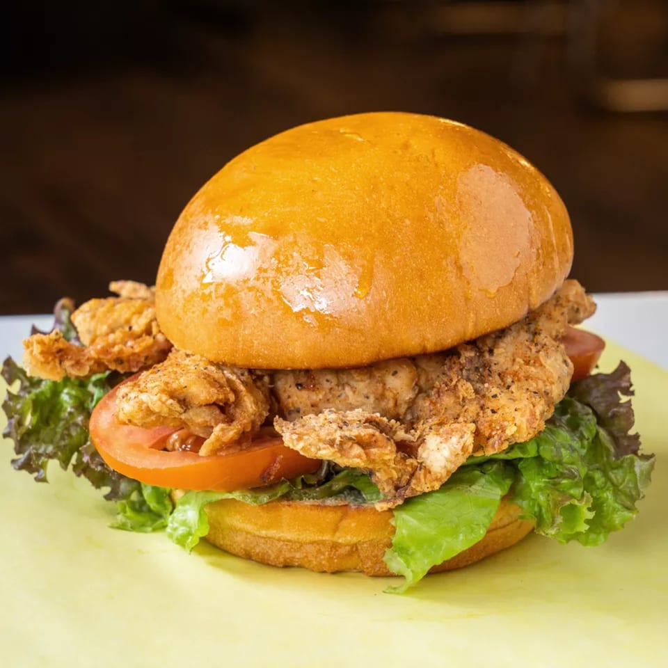 Crispy fried chicken sandwich with lettuce and tomato on a brioche bun, on a yellow surface.