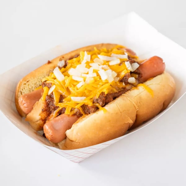 Two chili dogs with shredded cheese and diced onions in a paper tray.