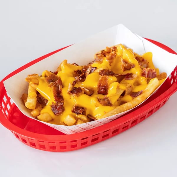 Golden french fries covered in melted yellow cheese and crispy bacon bits, served in a red basket.